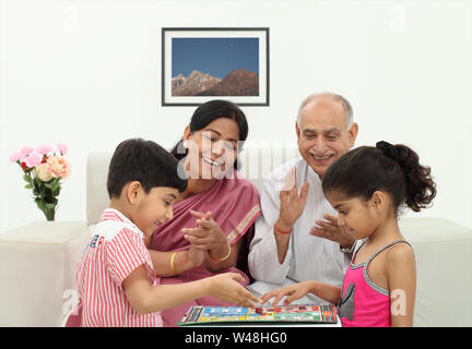 Junge und Mädchen spielen Ludo mit ihren Großeltern Stockfoto