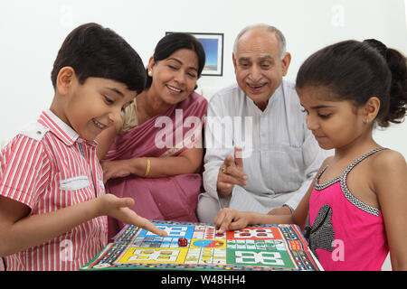 Junge und Mädchen spielen Ludo mit ihren Großeltern Stockfoto