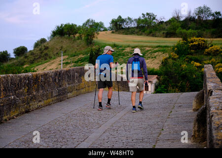 Pilger zu Fuß auf dem Camino de Santiago. Zwei Männer am frühen Morgen verlassen, überqueren Sie die Brücke, die nur alte Rock Light Pack mit Tage Notwendigkeiten Stockfoto