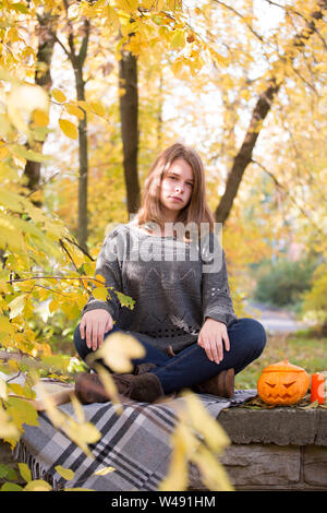 Schöne jugendlicher Mädchen im Herbst Garten saß auf dem Zaun, auf der Wolldecke plaid Decke mit Halloween Kürbis und Kerzen Stockfoto