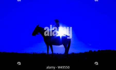 Silhouette einer Cowgirl auf offenen Ebene im Western Reiten ein Pferd beleuchtet durch die untergehende Sonne in Blau Stockfoto