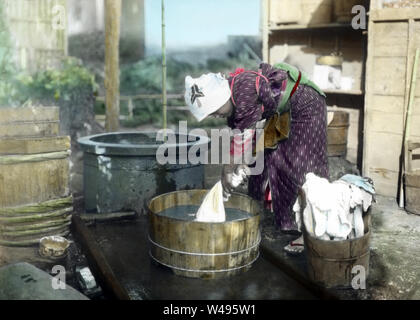 [1920s Japan - Japanische Frau die Wäsche machen] - eine Frau im Kimono ist Wäsche waschen mit Oke (holzbottiche) bei einer gut. 20. Jahrhundert vintage Glas schieben. Stockfoto