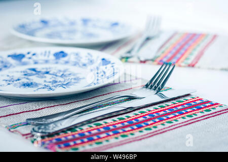 Tabelle Einstellung für Abendessen: weiß und blau Teller, Gabel, ein Messer auf einem gewebtem Stoff Serviette mit gesticktem Muster, traditionelle Handarbeit in der Ukraine Stockfoto