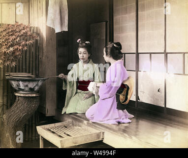 [1890s Japan - Japanische Frauen Waschen der Hände] - eine Frau im Kimono verwendet eine Hishaku (Löffel) Wasser über die Hände von einer anderen Frau, die ihre Hände waschen zu spritzen. Die zwei Frauen sitzen auf der Veranda eines privaten Hauses. Waschen der Hände (Temizu) ist ein wichtiges Reinigungsritual bei der Eingabe von Shinto Schrein gründen, sondern war auch nach Eingabe eines privaten Hauses. 19 Vintage albumen Foto. Stockfoto