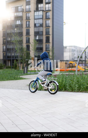 Sicherheit in einer modernen europäischen Stadt. Ein wenig glückliche junge fährt mit dem Fahrrad durch einen geschlossenen Innenhof in einem Mehrstöckigen städtischen Gebäude. Stockfoto