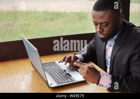 Schwarzer Mann ist die Zahlung der Bank Card auf dem Laptop. Online Shopping im Cafe sitzen. Junge afro-amerikanische Geschäftsmann kauft online seine Daten eingeben, um Computer von Kreditkarte, Seitenansicht. Guy Kunden. Stockfoto