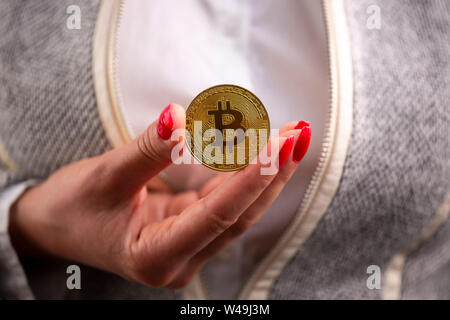 Virtuelle cryptocurrency Geld Bitcoin goldene Münze in der rechten Hand einer Frau mit rotem Nagellack. Die Zukunft des Geldes. Stockfoto