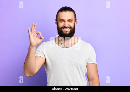 Einen schönen fröhlichen positiver Mann im weißen T-Shirt, das OK-Zeichen auf blauem Hintergrund isoliert. nach oben Porträt schließen. Körpersprache. gute Arbeit, alles Stockfoto