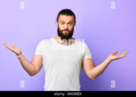 Junge starker, muskulöser Mann Unwissenheit angezeigt, zuckte mit den Schulter auf einem blauen Hintergrund. schöner Mann im weißen T-Shirt mit erhobenen Armen zweifelnd exresses Stockfoto