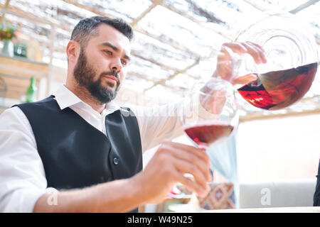 Junge Bartgeier Barkeeper oder Sommelier gießen Rotwein in wineglass Stockfoto