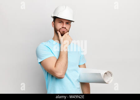 Nachdenklicher Mann mit der Hand am Kinn holding Blaupause in die Kamera schaut. verwirrte Mann in Hut. ernsten Kerl, die Idee, Plan. Mann, ein Problem zu lösen, Stockfoto