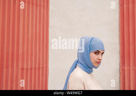 Junge muslimische Frau in Blau hijab stehend durch die Wand von Gebäude Stockfoto