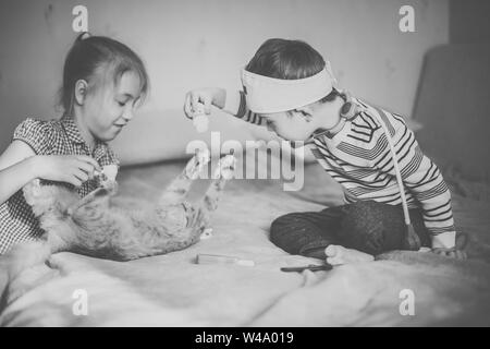 Kleinen Jungen in die Gläser mit Syndrom Dawn und blonde Mädchen spielen mit Spielzeug und Ginger cat. Schwarz und Weiß Stockfoto