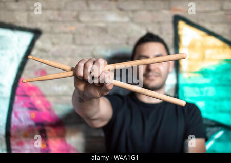 Hände von einem Schlagzeuger oder Musiker mit Trommelstöcken auf unscharfen Hintergrund auf eine Wand mit Graffiti. Mann mit Trommelstöcken auf städtischer Ort. Stockfoto