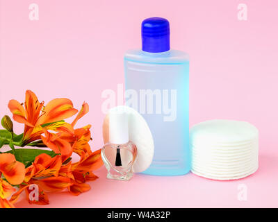 Glasflasche mit farblosem Nagellack, Kunststoff Flasche mit Nagellackentferner, Wattepads und orange Blumen auf einem Pastell rosa Hintergrund. Stockfoto