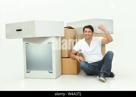 Mann, der mit Pappkartons sitzt und den Schlüssel zeigt Stockfoto
