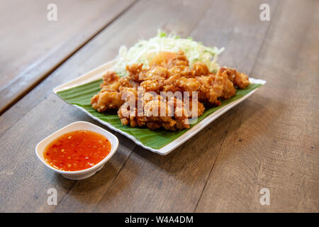 Knusprige Hähnchen Schenkel gegrillt im thailändischen Stil mit pikanter Sauce und Tomaten und Gemüse auf Green Banana leaf Stockfoto