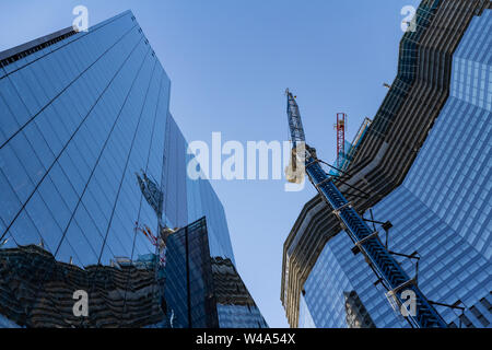 Modernes Gebäude im Bau an einem hellen, sonnigen Tag auf dem Hintergrund des blauen Himmels. Reflexion von Turmdrehkranen auf Windows Spiegel. Low Angle View Stockfoto