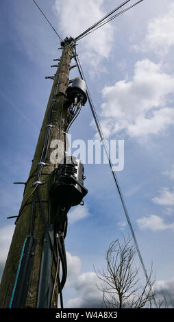 Ein britisches Holz- telegraphenmast gegen einen blauen Himmel mit Schritte, Telefon Kabel und altmodischen elektrischen Komponenten. Stockfoto
