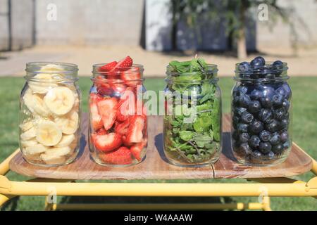 Nahaufnahme von Bananen, Erdbeeren, Minzblättern und Brombeeren in Gläsern auf einem Holzstuhl Stockfoto