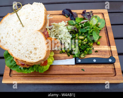 Café Mittagessen ein Huhn Cajun und Bacon Sandwich in Weißbrot mit Salat auf einem Holzbrett serviert. Stockfoto