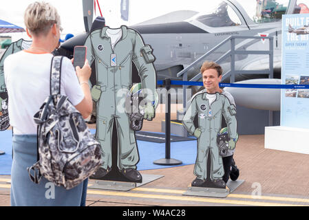 RAF Fairford, Gloucestershire, Großbritannien. Juli 2019. Die RIAT gilt als die weltweit größte Militärflugschau mit teilnehmenden Flugzeugen aus der ganzen Welt, mit über 30 Luftwaffen aus 20 verschiedenen Ländern im Jahr 2019. Erwachsener Besucher, der ein Foto mit einer Karikatur-Pilotenfigur mit Kinderausschnitt gemacht hat Stockfoto