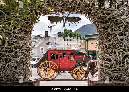 Ein Touristen Stagecoach der Elch Geweih Arch im George Washington Memorial Park, wie der Stadtplatz in Jackson Hole, Wyoming bekannt. Vier Bögen der Marktplatz sind ausschließlich von der lokalen Elchengeweihen gebaut. Jeder Bogen wird von einem Stahlgerüst unterstützt und von Hand mit mehr als 2.000 Geweih jeden gebaut. Die Bögen sind meist durch Reibung und Schwerkraft gehalten und müssen über alle 50 Jahre wieder aufgebaut werden. Stockfoto