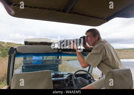 Männliche spiel Ranger über eine professionelle Kamera und nehmen Sie ein Foto der afrikanischen Tierwelt, während er auf die Tür der Safari 4x4 Spiel mit dem Fahrzeug fahren Stockfoto