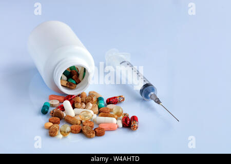 Tabletten und Kapseln sind von einer weißen Flasche auf eine weiße glatte Tisch in der Nähe einer Einwegspritze verstreut. Stockfoto