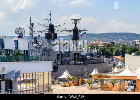 Varna, Bulgarien, 20. Juli 2019. Das Gebäude des Meeres von Varna auf dem Hintergrund einer großen, grauen moderne Kriegsschiff an einem sonnigen Sommertag. Stockfoto