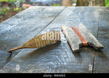 Alte Griff für vertikale blinken Raubfische. Kupfer geschmiedet Spinner und Haspel mit Seil auf Holz- rustikalen Hintergrund. Stockfoto