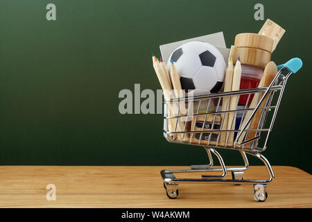 Shopping Cart mit Schulmaterial über schiefertafel Hintergrund. Zurück zu Schule verkauf Konzept Stockfoto