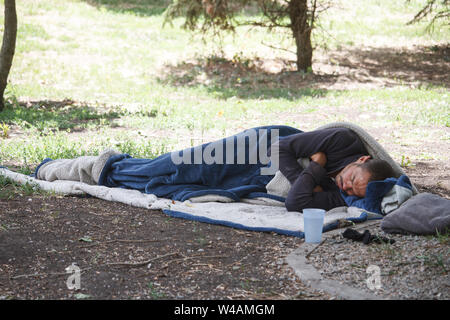 Charkow, Ukraine - 30. Juni 2019: Ein einsamer Touristische versteckte im Schlafsack und schläft auf dem Boden in einem Stadtpark, einem Obdachlosen schläft im aftern Stockfoto