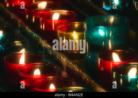 Nahaufnahme der Zeilen von Kerzen brennen in bunten Glas Teelichter in einer Kirche. Stockfoto