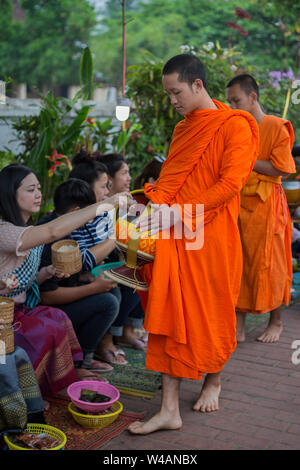 Menschen Almosen, die für Junge buddhistische Mönche auf der Straße in den frühen Morgenstunden in Luang Prabang, Laos. Das Ritual ist Tak Bat genannt. Stockfoto