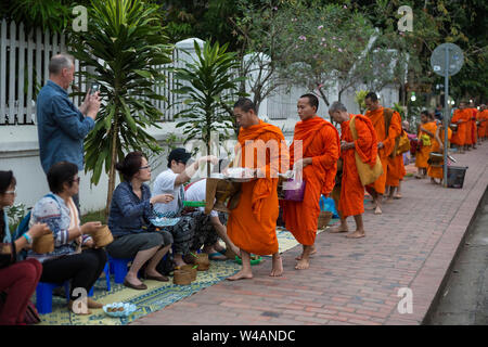 Menschen Almosen zu geben, buddhistische Mönche auf der Straße in den frühen Morgenstunden in Luang Prabang, Laos. Das Ritual ist Tak Bat genannt. Stockfoto