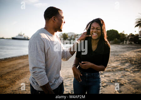 Vater und Tochter lachen und spielen am Strand bei Sonnenuntergang Stockfoto