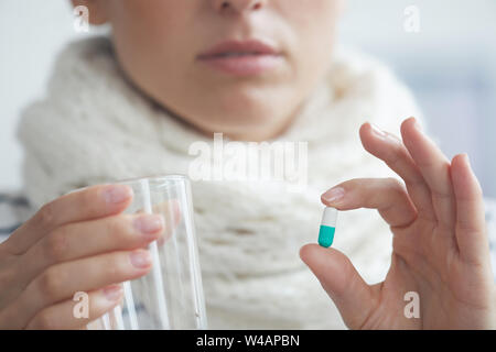 Nahaufnahme der jungen Frau im warmen Schal um den Hals hält Glas Wasser und nehmen Virostatika Stockfoto
