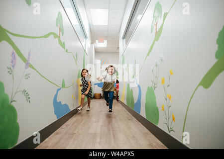 Zwei kleine Mädchen lächeln und führen Sie ein Wandbild überdachten Halle in einer Schule Stockfoto
