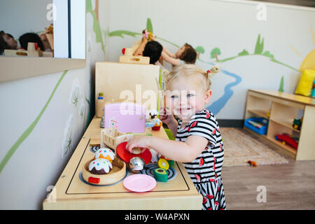 Blond kleinkind Mädchen Lächeln für die Kamera, als sie sich mit Spielzeug Herd spielt Stockfoto