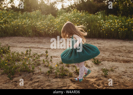 Kleines Mädchen twirling ihr Kleid in der Hintergrundbeleuchtung und der Blumen Stockfoto