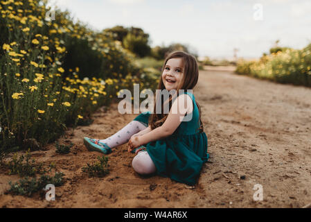 Kleine Mädchen spielen in einem Blume Bereich mit blauem Himmel hinter ihr Stockfoto