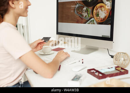 Nahaufnahme der lächelnde Frau am Tisch sitzen und mit ec-Karte während der Bestellung food online über die Website Stockfoto
