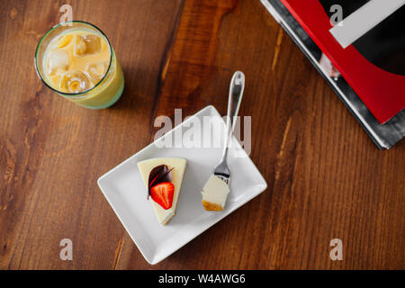 Ein Stück leckeren Käsekuchen mit Erdbeeren auf die Oberseite. Kalte frappe mit Eis neben, Ansicht von oben. Stockfoto