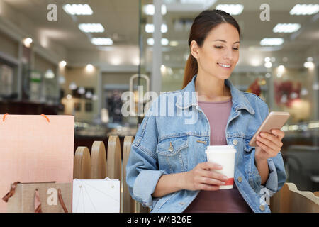 Lächelnd attraktive junge Frau mit Kaffeepause auf der Werkbank während langer Shopping in der Mall Stockfoto