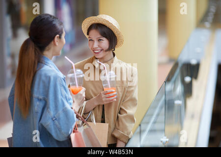 Glücklich, aufgeregt, gesprächig weiblichen Käufern in den casual Outfits am Geländer in Mall und süße Getränke genießen. Stockfoto