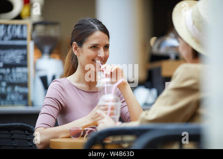 Positive stilvolle Damen am Tisch im Café trinken und erfrischende Getränke sitzen beim Chatten Stockfoto