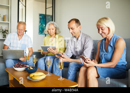 Gruppe der zeitgenössischen ältere Leute über verschiedene Geräte auf dem Sofa zu Hause sitzen, kopieren Raum Stockfoto