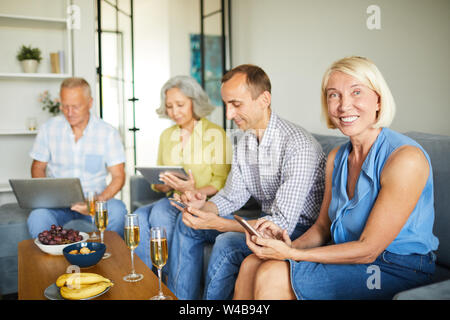 Gruppe der zeitgenössischen ältere Leute mit verschiedenen Internet Devices auf dem Sofa zu Hause sitzen, kopieren Raum Stockfoto