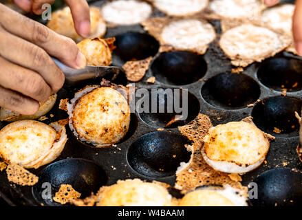 Mörtel - geröstete Gebäck oder "Kanom Krok' ist für traditionelle thailändische Dessert. Frau Hand entfernen Kanom Krok von Herd durch die Löffel. Street Food in Thailand. Thai Stockfoto